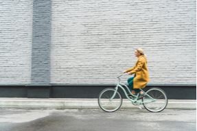 A woman in a yellow coat, cycling in the city as a form of exercise and self care to help stave off pain from varicose veins and venous insufficiency
