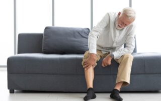 Older man sitting on a couch rubbing his lower leg from restless legs discomfort