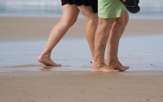 Older couple walking on the beach in summer, managing vein symptoms in the heat